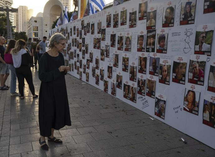 An Israeli woman looks at photos of Israelis missing and held captive in Gaza, displayed on a wall in Tel Aviv